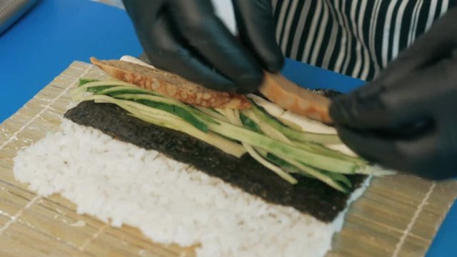 Close-up of professional chef's hands in black gloves making sushi and rolls in a restaurant kitchen. Japanese traditional food. Preparation process. step by step