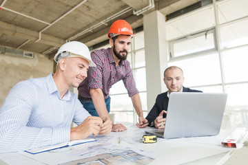 male engineers, architects working at the desk in helmets. Drawings, laptop, roulette on the...