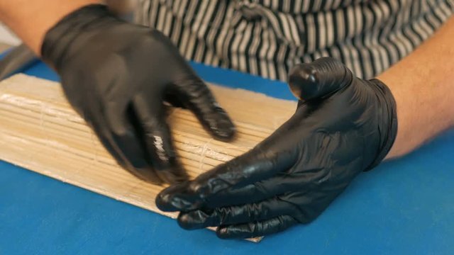 Close-up of professional chef's hands in black gloves making sushi and rolls in a restaurant kitchen. Japanese traditional food. Preparation process. step by step