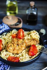 grilled chicken leg and pasta in a pan with vegetables and spices on a wooden board