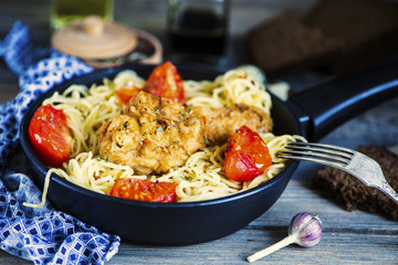 grilled chicken leg and pasta in a pan with vegetables and spices on a wooden board