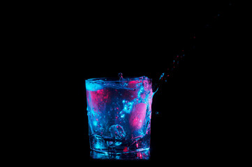 Pouring from the side and splashing in a rocks glass under blue and red lights isolated on a black background