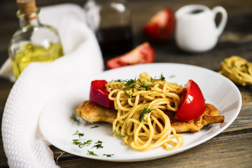 pasta and fried meat with spices and vegetables on a wooden board
