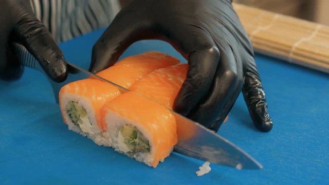 Close-up of professional chef's hands in black gloves making sushi and rolls in a restaurant kitchen. Japanese traditional food. Preparation process. step by step