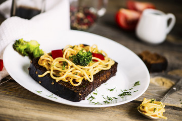 fried black bread with spaghetti and vegetables on a plate on a wooden table