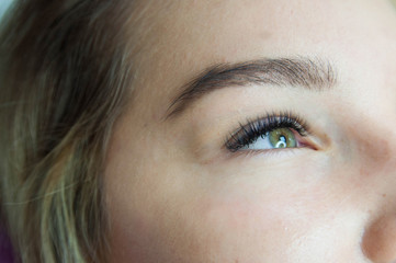 Fototapeta premium Eyelash extension procedure. Young beautiful woman eye with long false eyelashes. Close up macro shot of fashion eyes in beauty salon.