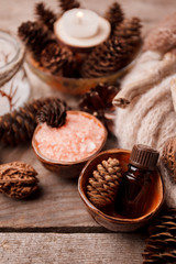 Fototapeta na wymiar Spa and wellness setting with sea salt, oil essence, cones and candle, wooden decor on wooden background. Fall autumn winter wellness concept, Relax and treatment therapy.