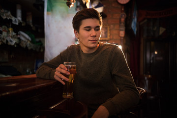 Young man drinking beer at the bar, looking to the side
