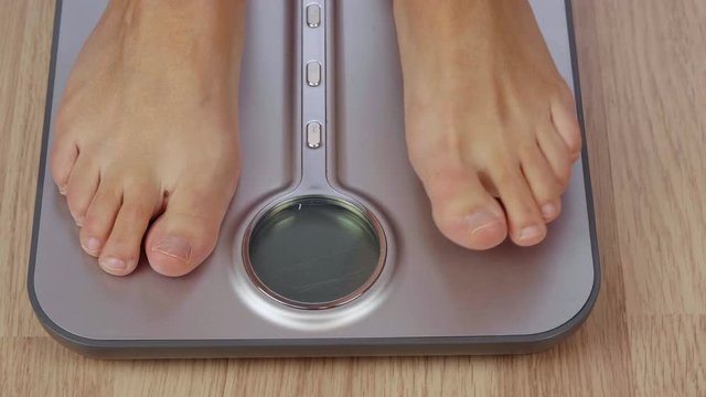 Partial view of barefoot woman weighting on electronic scale with display