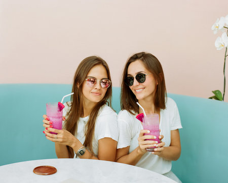 Lovely ladies wears similar straw hats having fun together enjoying icy fruit cocktails in summer day.