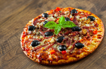 Pizza with Mozzarella cheese, salami, pepper, ham, pepperoni, olives, Spices and Fresh Basil. Italian pizza on wooden background