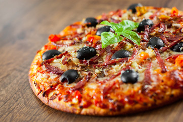 Pizza with Mozzarella cheese, salami, pepper, ham, pepperoni, olives, Spices and Fresh Basil. Italian pizza on wooden background