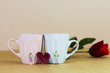 miniature couple with red heart shape on wooden floor, blue and pink coffee cup, rose flower, Image for Love couple concept.