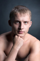 Fototapeta premium Muscular blonde young handsome man topless, brow furrowed, fist near face, looks straight, biceps, sportsman, studio light, low key, black background, close up