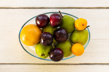 Fresh fruit in a bowl lying on a wooden table from a top view