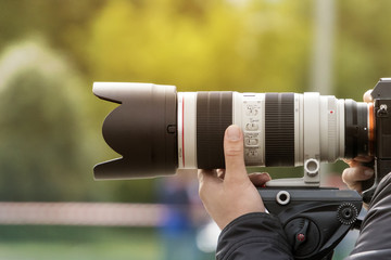 Handshot of a professional photographer outdoors. Man holds a modern camera device. Cameraman...
