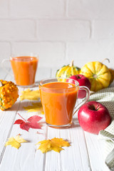 Seasonal autumn thanksgiving concept. Pumpkin fresh juice drink cocktail on a white table with fall maple leaves. Copy space