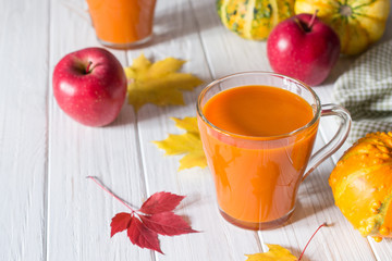 Seasonal autumn thanksgiving concept. Pumpkin fresh juice drink cocktail on a white table with fall maple leaves. Copy space