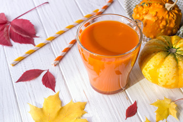 Fresh pumpkin juice in glass cup, pumpkins and fallen maple leaves. Fall drink concept
