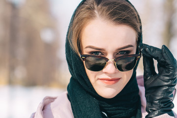 Close up portrait of a young woman outdoors looking over her sunglasses. Sunny winter day.