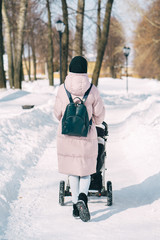 Young mother wlalking with a newborn child in the park in winter. Sunny winter day walk.