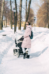 Young mother wlalking with a newborn child in the park in winter. Sunny winter day walk.