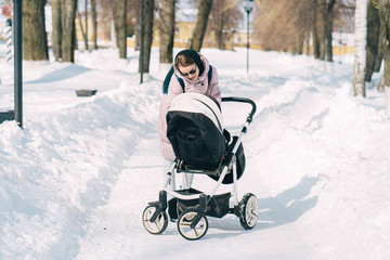 Young mother wlalking with a newborn child in the park in winter. Sunny winter day walk.