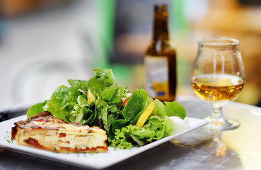 Traditional French food: quiche lorraine and fresh salad leaves with glass of beer on background