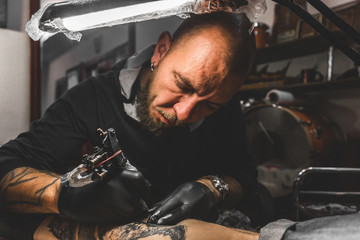 The tattoo artist creates a picture on the body of a man. close-up of tattoo machines and hands