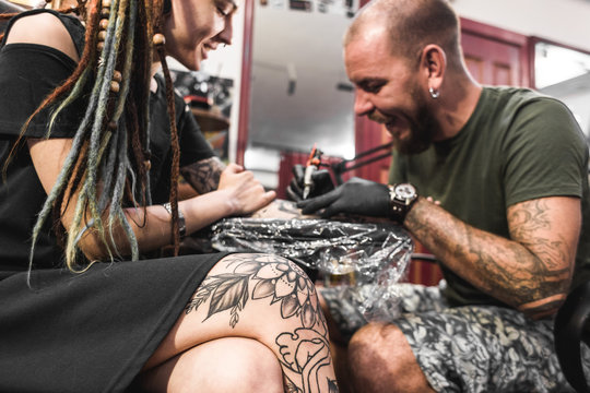 girl with dreadlocks in a tattoo parlor. The master creates a picture on the body of a young beautiful girl. Close-up of hands and tattoo machine