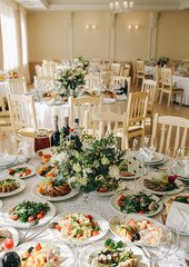 Beautifully set round tables at the restaurant. Delicious food at the wedding reception. White tablecloths and flowers decorations. Elegant space in the big hall. Happy celebration. Vertical photo.