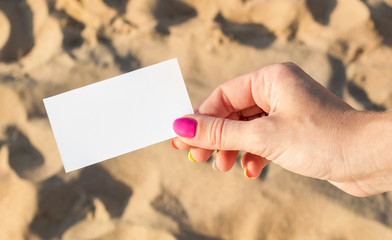 Woman holding blank card against sand of beach.