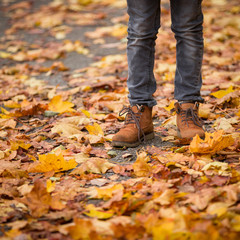 Closeup of toddler's legs in orange shoes on bright autumn leaves background. The child walks in the park. Maple leaves of different colors, yellow, red, orange. Lifestyle concept