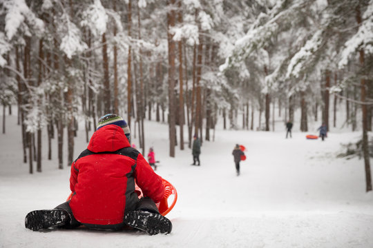 Back view on a kid boy in warm clothes sitting on snow and ready to slide down the hill. Activities with children outdoors.