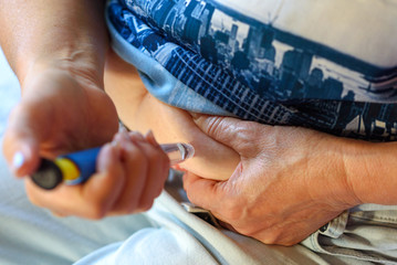 Elderly woman giving herself injection in abdomen against pain and discomfort in home. Old senior woman used Pen Injector indoor. Health Technology, healthy lifestyle concept.