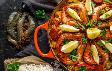 Traditional paella in the fry pan with chicken, prawns, spicy chorizo, lemon and glass of white wine.