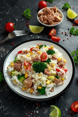 Fresh Tuna rice salad with sweet corn, cherry tomatoes, broccoli, parsley and lime in black bowl