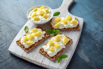 Homemade Crispbread toast with Cottage Cheese and Pineapple on white wooden board.