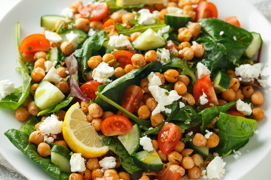 Chickpeas Salad with cucumber, tomatoes, feta cheese and green mix in a white plate. healthy food.