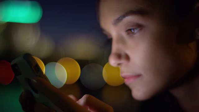 Closeup Of Woman Using Her Smartphone, Her Face Is Beautifully Illuminated By The Screen, Colorful City Lights In Background