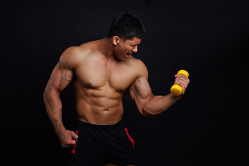 Muscular frustrated angry guy doing exercises with dumbbell over black background. studio...