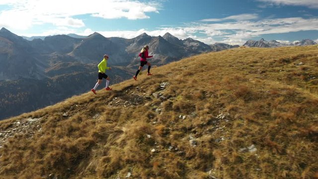 4K sport footage, aerial view 44 years old woman and 46 years old man trail running together high up in autumn mountains

