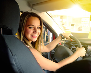 Portrait of young smiling woman siting behind steering wheel inside car