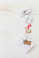 Top view on nice Christmas gifts wrapped in white gift paper, Christmas tree decorations on white wooden background with sparkling stars. New Year, holidays and celebration concept