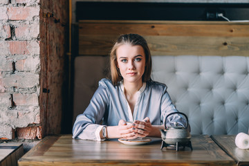 Beautiful young woman sits near big window at cafe, drinks hot tasty beverage, thinks about future plans.