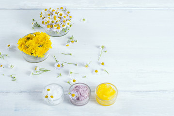 cosmetic product samples with herbal flowers on white wooden table