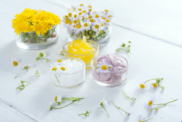 cosmetic product samples with herbal flowers on white wooden table