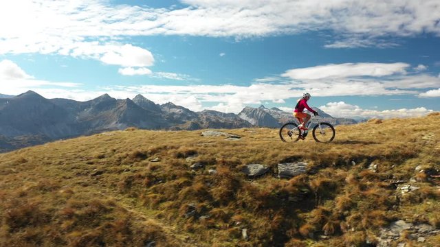 4K sport footage, aerial view one woman riding electric mountain bike over ridge high up in mountains panorama on sunny autumn day
