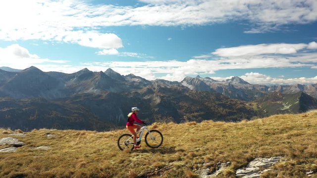 4K sport footage, aerial view woman riding electric mountain bike over ridge high up in mountains on sunny autumn day
