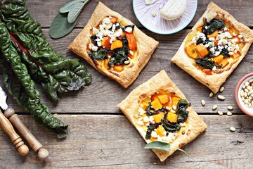 Fototapeta premium Pumpkin, chard, goat cheese and pine nuts puff pastry tarts. Overhead view